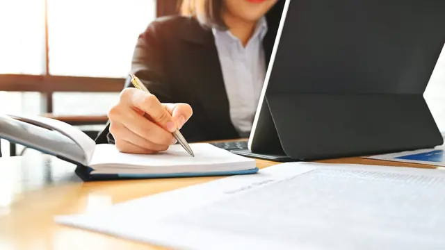 Compliance reviewer making notes beside audit documents
